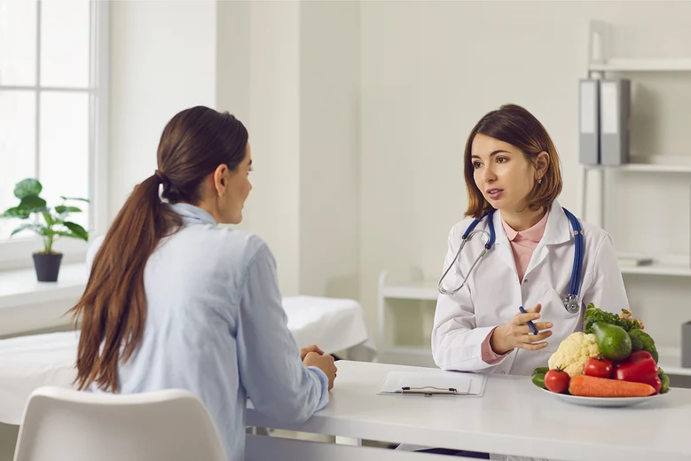 Ernährungsberatung durch Diätassistentin: Ärztin mit Stethoskop erklärt Patientin ausgewogene Ernährung mit frischem Gemüse. Diätassistenten beraten bei Diabetes, Allergien und Übergewicht, erstellen individuelle Ernährungspläne.
