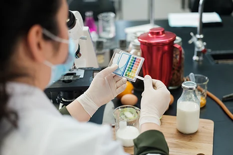 Lebensmittelchemikerin analysiert mit Farbskala Milchproben im Labor mit Mikroskop. Lebensmittelchemiker untersuchen Lebensmittel auf Qualität, Inhaltsstoffe, Schadstoffe und Kennzeichnung zum Schutz der Verbraucher und Einhaltung gesetzlicher Vorgaben.