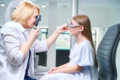 Augenoptikerin untersucht Mädchen mit Messbrille und Ophthalmoskop. Augenoptiker führen Sehtests durch, messen Sehstärke, beraten zu Brillen und Kontaktlinsen und passen Sehhilfen individuell an für optimale Sehkorrektur bei Kindern und Erwachsenen.