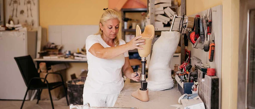 Orthopädiemechanikerin passt Beinprothese in Werkstatt an. Orthopädiemechaniker fertigen und reparieren Prothesen, Orthesen und Hilfsmittel, nehmen Maß, passen individuell an und verbessern Mobilität und Lebensqualität von Menschen mit Einschränkungen.