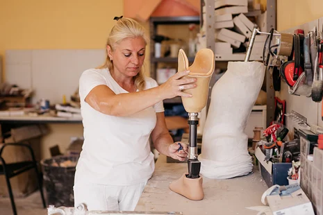 Orthopädiemechanikerin passt Beinprothese in Werkstatt an. Orthopädiemechaniker fertigen und reparieren Prothesen, Orthesen und Hilfsmittel, nehmen Maß, passen individuell an und verbessern Mobilität und Lebensqualität von Menschen mit Einschränkungen.