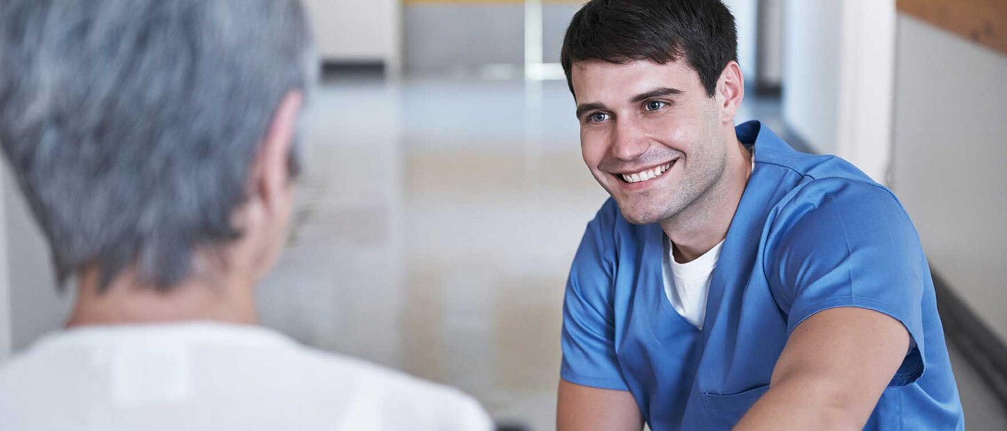 Pflegefachkraft guckt Patienten an und lächelt.