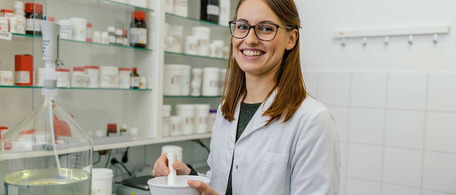 Pharmazeutin steht in Apotheke und lächelt in die Kamera.