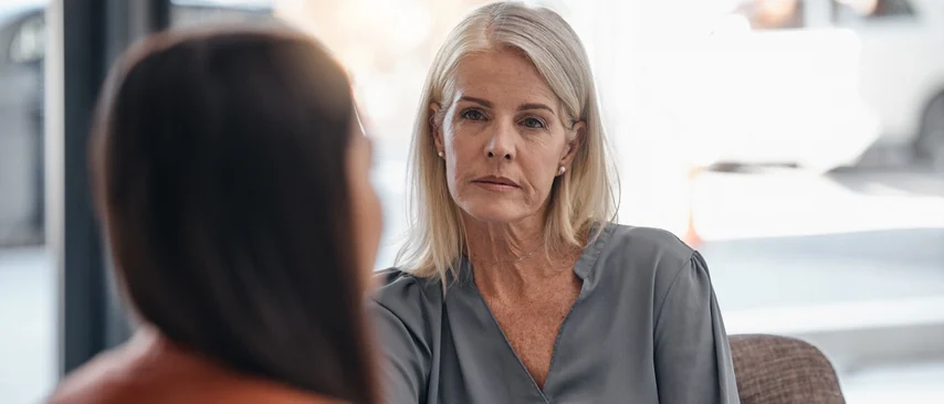 Psychotherapeutin im therapeutischen Gespräch mit Patientin, beide sitzen sich gegenüber in ruhiger Gesprächsatmosphäre.