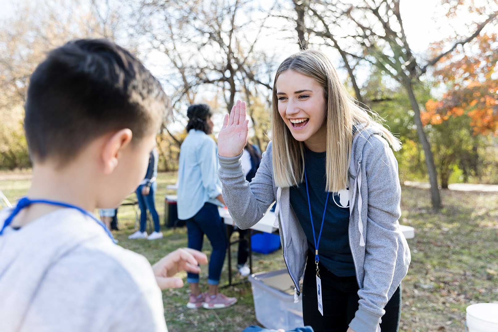 Sozialarbeiterin beugt sich zu Jungen und hebt ihre Hand für ein High five.