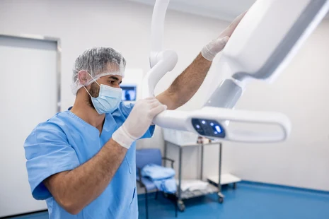 Medizinisch-technischer Assistent (MT) positioniert Röntgengerät im sterilen OP-Raum. MT-Berufe umfassen Radiologie, Laboranalytik und Funktionsdiagnostik mit bildgebenden Verfahren, Laboruntersuchungen und medizintechnischen Diagnosen.