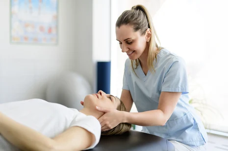 Massagetherapie: Therapeutin behandelt Patientin mit Nackenmassage. Masseure und medizinische Bademeister führen Massagen, Bewegungstherapien und physikalische Anwendungen zur Schmerzlinderung und Rehabilitation durch.