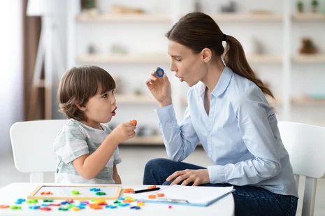 Logopädin bei Kindertherapie: Therapeutin übt mit Jungen spielerisch Artikulation durch Blasen bunter Ringe. Logopäden behandeln Sprach-, Sprech- und Schluckstörungen, fördern Wortschatz und Sprachentwicklung.