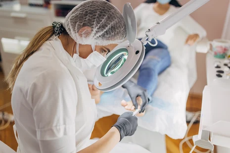 Podologin mit Lupenleuchte bei medizinischer Fußbehandlung. Podologen behandeln Fußerkrankungen wie Hornhaut, Nagelveränderungen und diabetischen Fuß, führen therapeutische Maßnahmen durch und verordnen orthopädische Hilfsmittel.