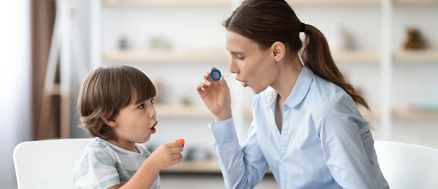 Logopädin übt spielerisch mit Kleinkind Lautbildung mithilfe bunter Therapiewerkzeuge. Sprachtherapie für Kinder: Logopäden fördern altersgerechte Sprachentwicklung, Artikulation und Kommunikationsfähigkeit durch kindgerechte, spielerische Übungsmethoden.