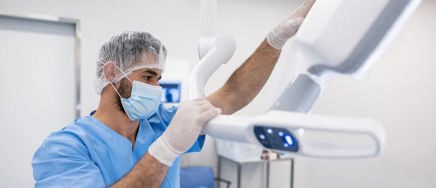 Medizinischer Technologe mit Haube und Maske bedient Röntgengerät. MT für Radiologie erstellen diagnostische Röntgen-, CT- und MRT-Aufnahmen, positionieren Patienten, bedienen bildgebende Geräte und gewährleisten Strahlenschutz bei medizinischen Untersuch